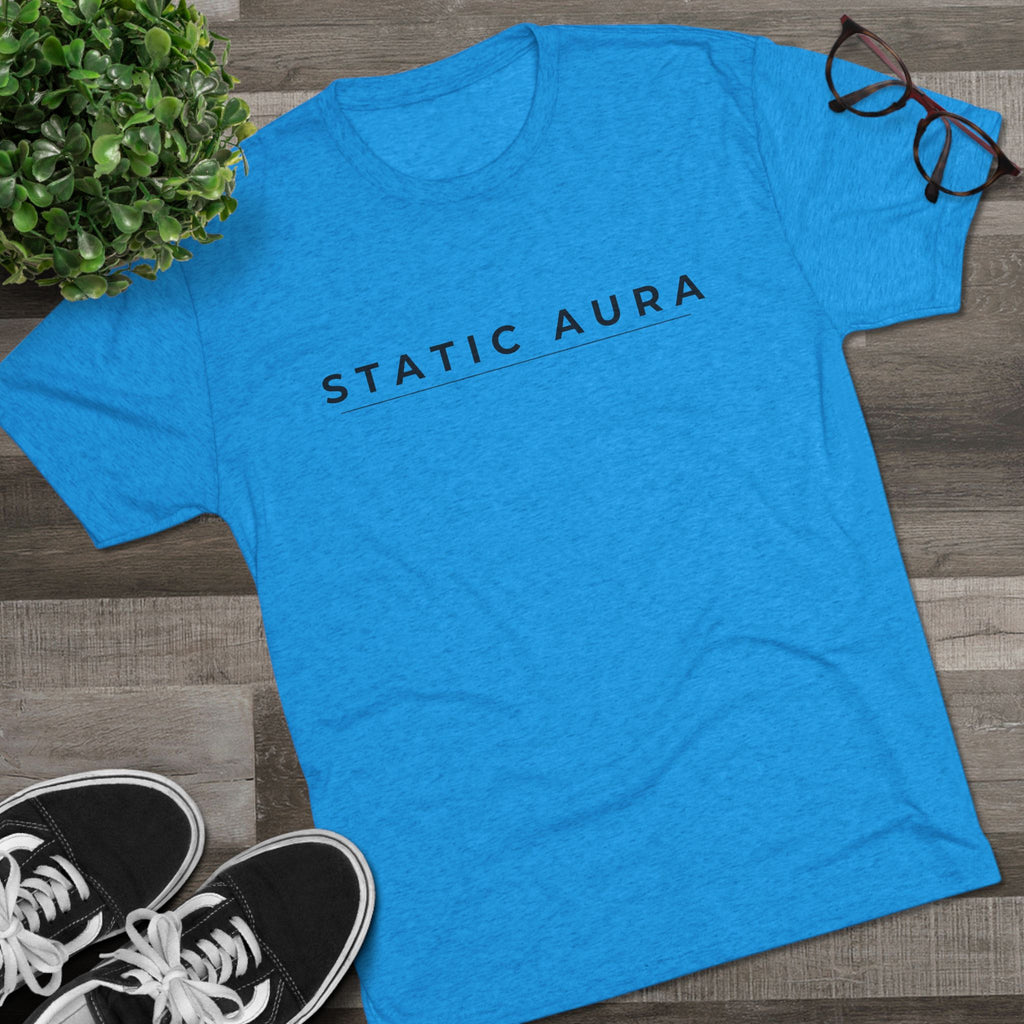 Blue t-shirt with a logo on a wooden surface next to sneakers and a plant