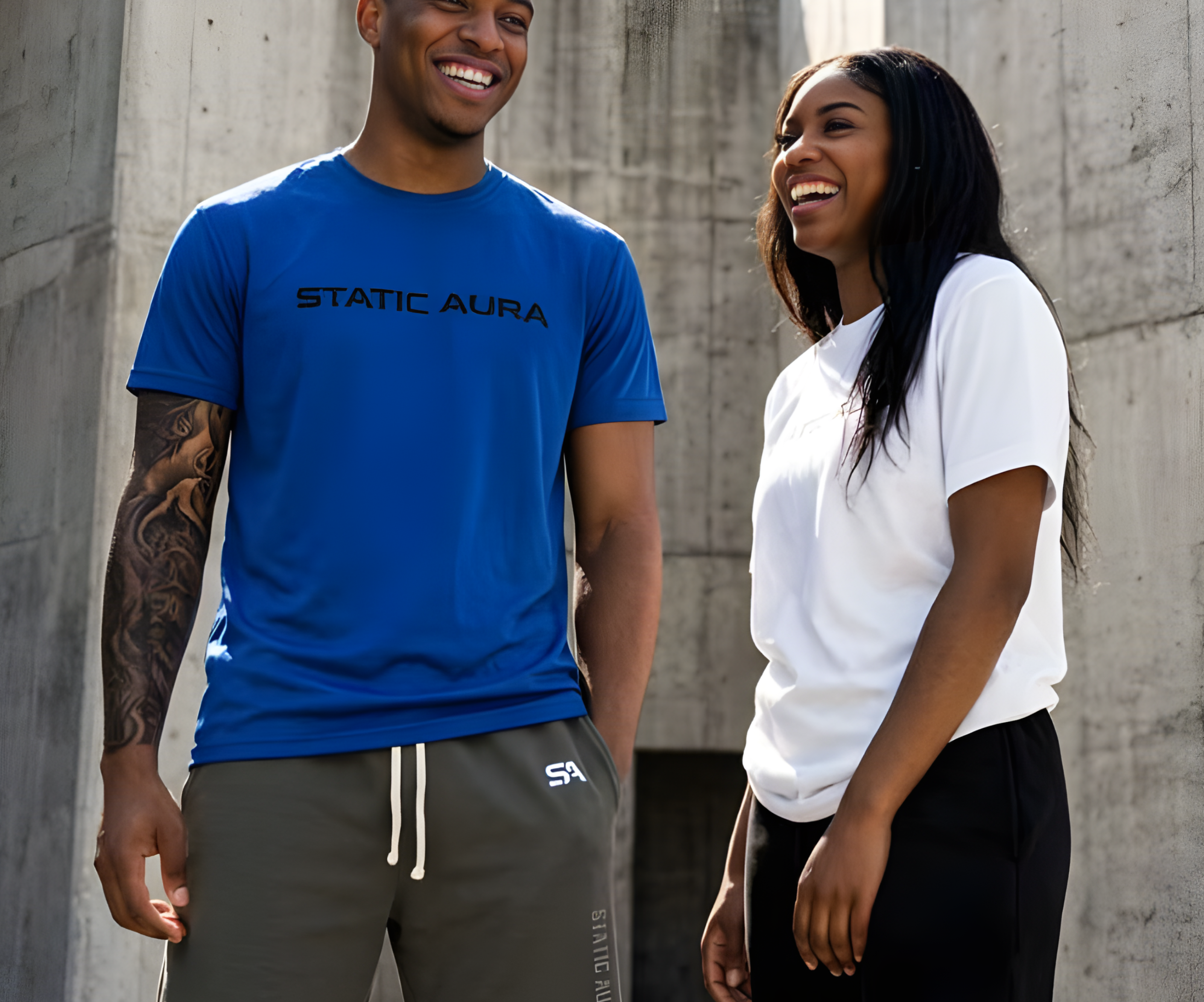 Two people standing in front of concrete structures, one wearing a blue 'Static Aura' t-shirt and gray shorts, the other in a white t-shirt and black pants.
